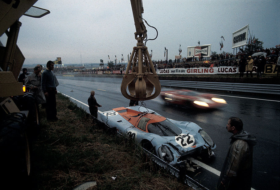 The destroyed Porsche 917K 026 of David Hobbs (GB) and Mike Hailwood (GB) is being removed from track after lap 49 whilst a Ferrari passes by