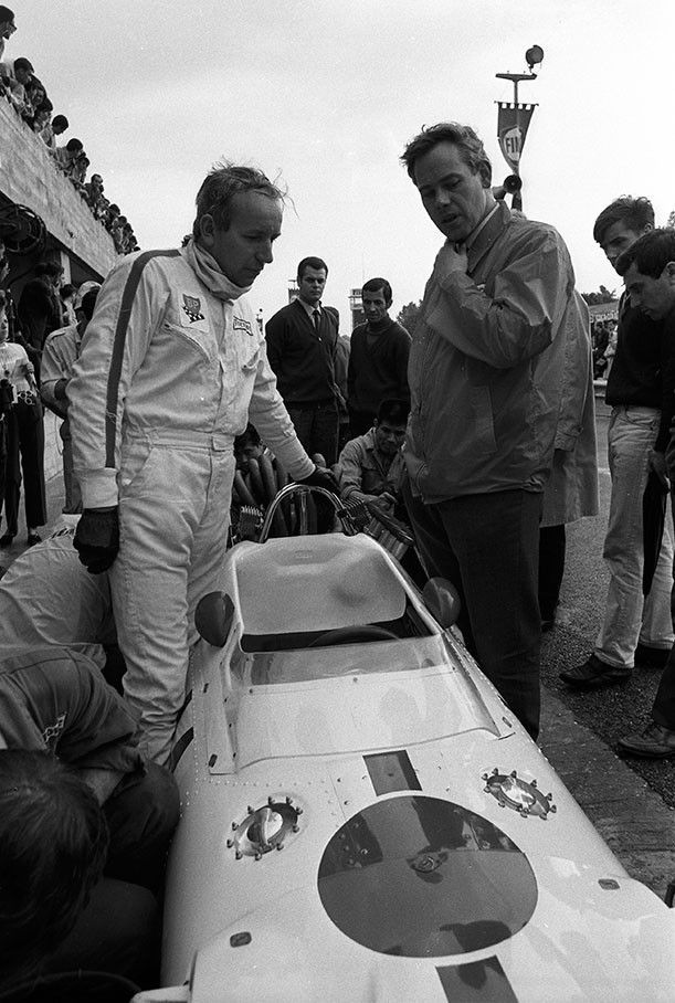 Whilst mechanics prepare his Honda RA300 car, later race winner John Surtees chats with Keith Duckworth