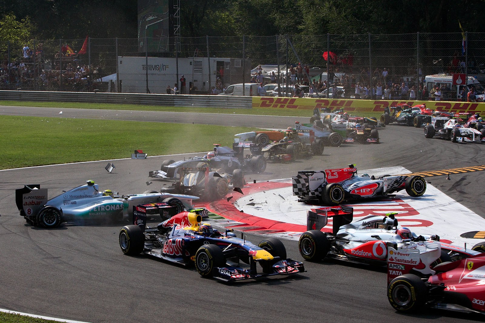 The start field squeezes through turn one as a powerless Vitantonio Liuzzi of HRT slides over the lawn into the queue and ends the race for Rosberg, Petrov and nearly Barrichello
