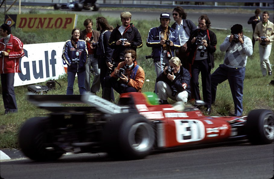 Photographers standing close to action, while Henrie Pescarolo (March Ford-Cosworth) passes by.