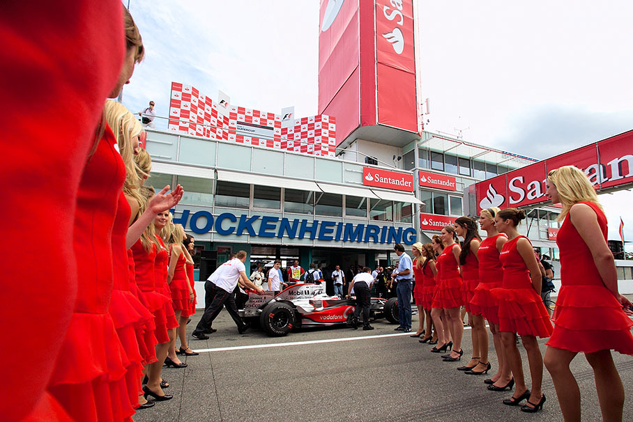 A McLaren car is being rolled through the phalanx of grid girls