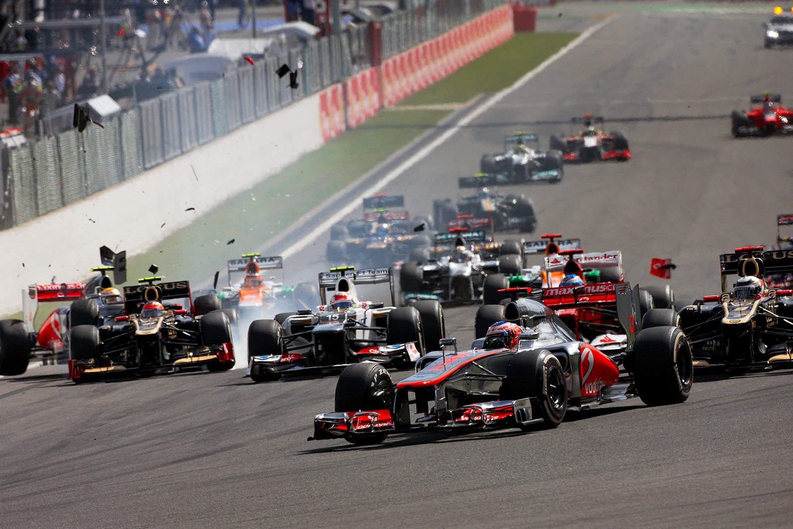 At the start of the Belgian Grand Prix 2012, the start field approaches turn one with pole setter Button in front of Raikkonen, Romain Grosjean and Lewis Hamilton collide on the left