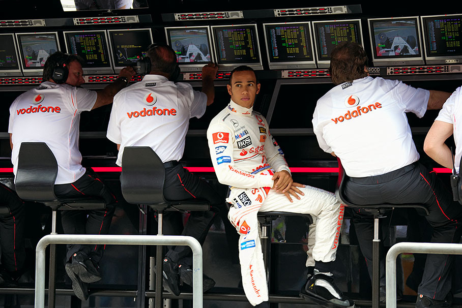 Lewis Hamilton sits at pitwall command center between Ron Dennis and Norbert Haug