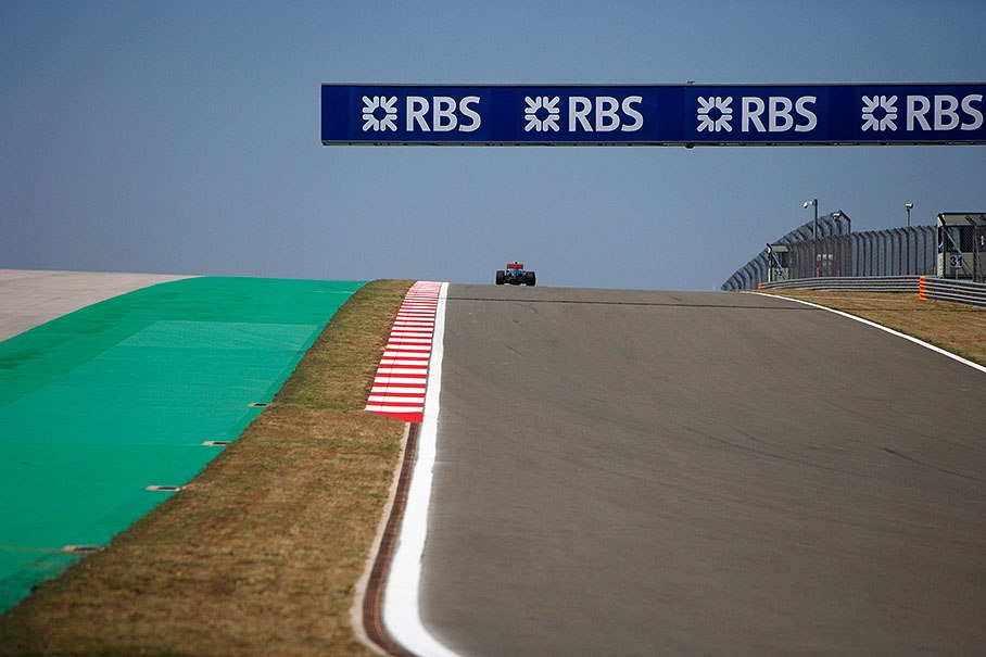 A McLaren racecar on top of the hill behind turn 11