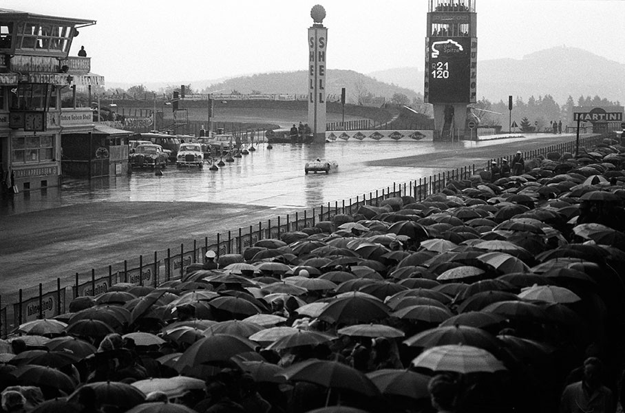 A field of umbrellas on the main grandstand watch the cars racing through the rain