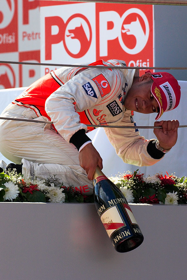 Lewis Hamilton shares his bottle of champagne with the team and lets it fall from the podium