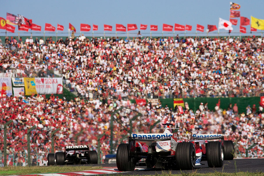 Three Japanese cars dueling in front of a huge filled-up flagged grandstand