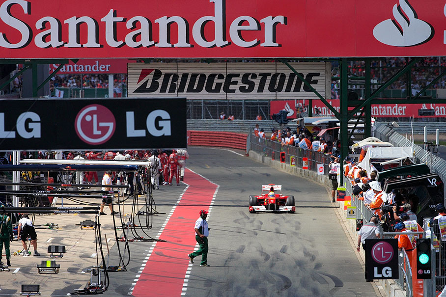 Lotus Racing's Tony Fernandes hurries over the pit lane in front of Ferrari's Felipe Massa who pits with a punctured right rear tyre after a touch with team mate Alonso in lap one