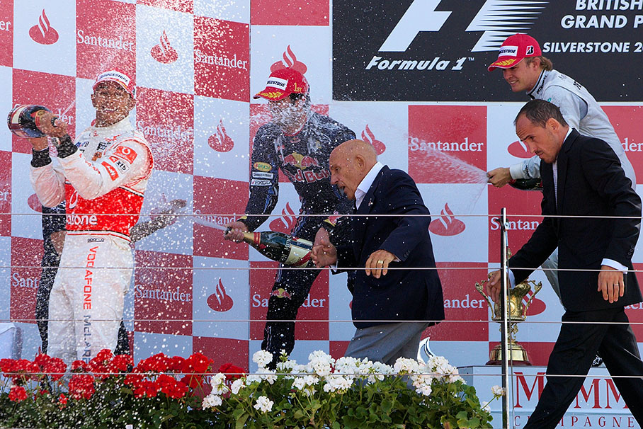 Sir Stirling Moss flights the champagne showers on the podium of the British GP 2010