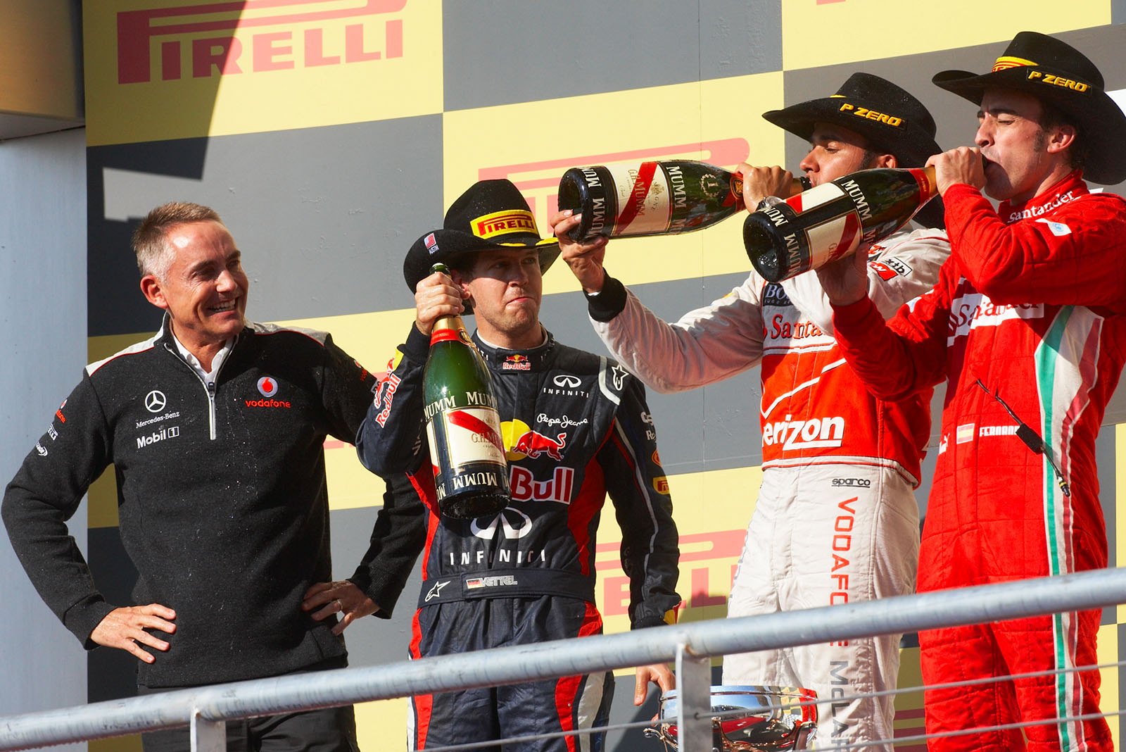 McLaren team principal Martin Whitmarsh watches the champagne flowing for the fastest cowboys: second placed Sebastian Vettel of Red Bull, McLaren's winner Lewis Hamilton and third placed Fernando Alonso of Ferrari