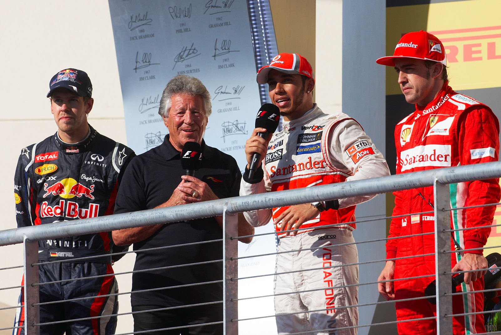 Mario Andretti, Italian racing multitalent and 1978 Formula 1 World Champion, interviews second placed Sebastian Vettel of Red Bull, McLaren's winner Lewis Hamilton and third placed Fernando Alonso of Ferrari on the podium